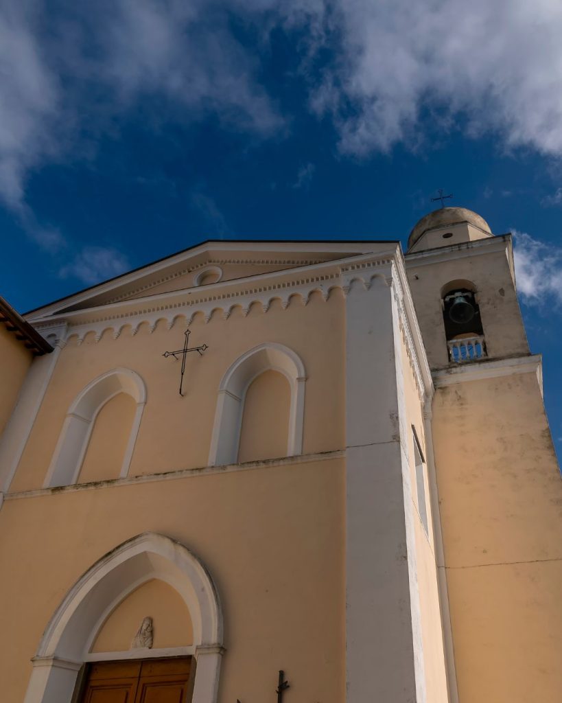 Facciata della Chiesa di Santa Lucia a Luciana, nel comune di Fauglia, fotografata dal basso con il campanile e il cielo azzurro sullo sfondo.